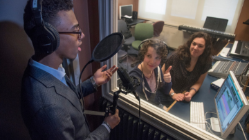 Student sings into microphone in recording studio. 