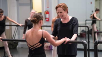 Professor works with student at ballet barre. 