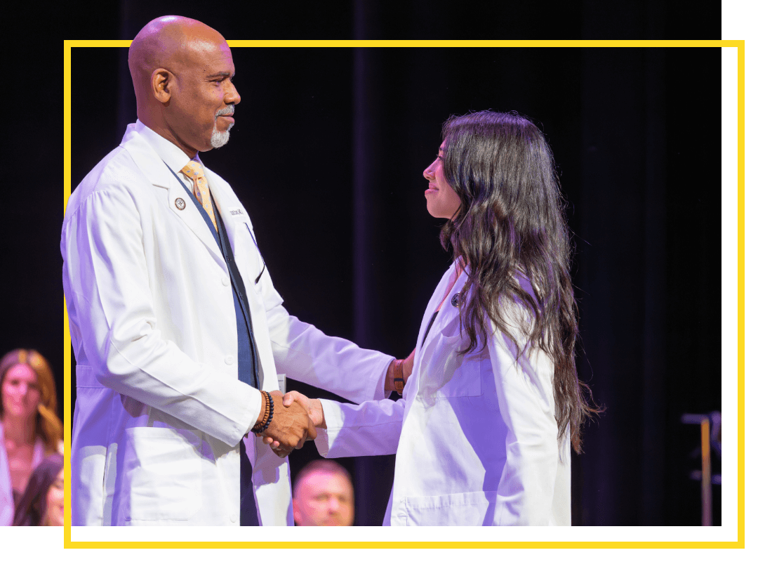 A healthcare student shaking hands with a faculty member at a ceremony