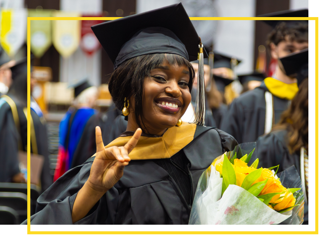 A Bonnie at graduation, holding up an affectionate hand sign and flowers